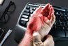 senior man holding wrist over keyboard with carpal tunnel pain indicated in red.