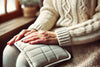 close-up of senior in white knit sweate rusing a heating pad on their knees.